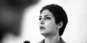 Black-and-white tight close-up of the vocalist mid-phrase with a microphone in the foreground and a focused expression.