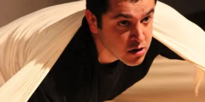 Nima Nazarinia on stage in TAN, wrapped in sheets.